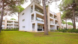 Un moderno edificio de varios pisos con balcones, rodeado de un césped cuidado y árboles.