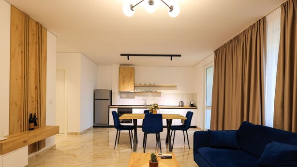 Una sala de estar moderna con un sofá azul, una mesa de centro de madera y un comedor con una mesa y sillas de madera.