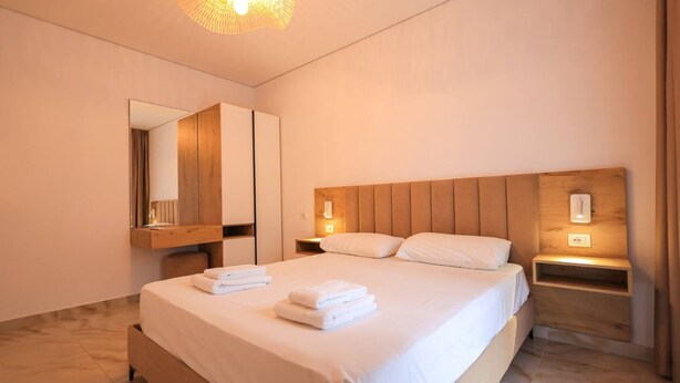 Une chambre d’hôtel moderne avec un grand lit, une tête de lit en bois, des tables de chevet et un miroir.