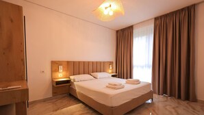 Una habitación de hotel moderna con una cama grande, cabecera de madera, mesitas de noche con lámparas y vistas al exterior a través de amplias ventanas.