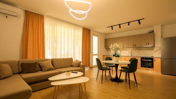 Un salon moderne comprenant un canapé, une table à manger et des chaises. Il y a également un coin cuisine avec des placards et un réfrigérateur.