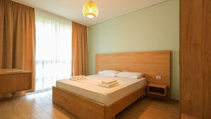 Une chambre moderne avec un lit en bois, une table de chevet, un luminaire suspendu et une vue sur l’extérieur grâce à de grandes fenêtres.