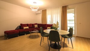 Ein modernes Wohnzimmer mit einem roten Ecksofa, einem runden Esstisch mit Stühlen und einer Deckenleuchte.