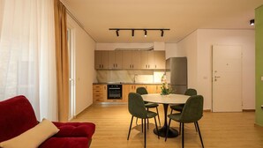 Eine moderne Küche mit Holzschränken, einem Einbauofen und einem Essbereich mit rundem Tisch und grünen Stühlen.