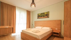 Ein Schlafzimmer mit einem hölzernen Bett, einem Nachttisch, einem Schreibtisch und einem Gemälde von Tukane.