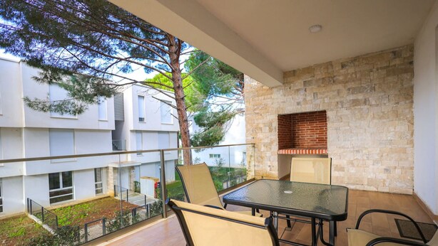 Ein Balkon mit Glastisch und -stühlen, einer Steinmauer und Blick auf ein Gebäude mit einem Baum.