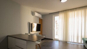 A modern living room with a flat-screen TV mounted on the wall, a sliding glass door leading to a balcony, and a minimalist furniture arrangement. - Sanpietro Vacation Apartment 030 (Ishëm)