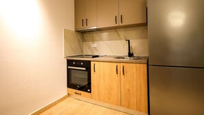 A compact kitchen with a built-in oven, a stainless steel refrigerator, and wooden cabinets. - Sanpietro Vacation Apartment 038 (Ishëm)