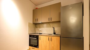 A compact kitchen with a built-in oven, a stainless steel refrigerator, and wooden cabinets. - Sanpietro Vacation Apartment 038 (Ishëm)