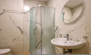 Ein Badezimmer mit Duschkabine aus Glas, einem weißen Waschbecken und einer Wand mit Marmorfliesen.