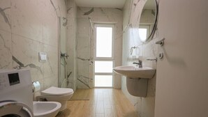 Une salle de bain avec un mur en marbre, une douche, des toilettes, un lavabo et un lave-linge.