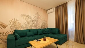 Una sala de estar con un sofá verde, una mesa de centro de madera y una pared con diseños de hojas de palma.