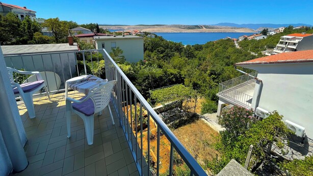 Un balcón con vista al mar, rodeado de vegetación y edificios.