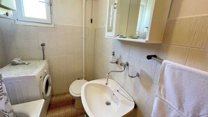 Un baño con lavadora, inodoro, lavamanos y un perchero para toallas.
