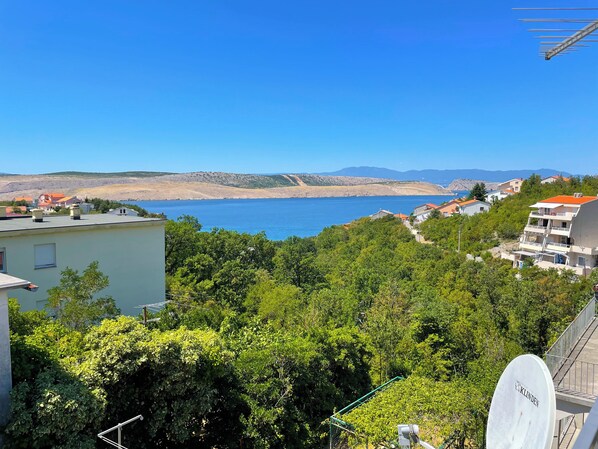 A coastal residential area with houses, a satellite dish, and a clear view of the sea and distant mountains. - Apartment Asta (Jadranovo)