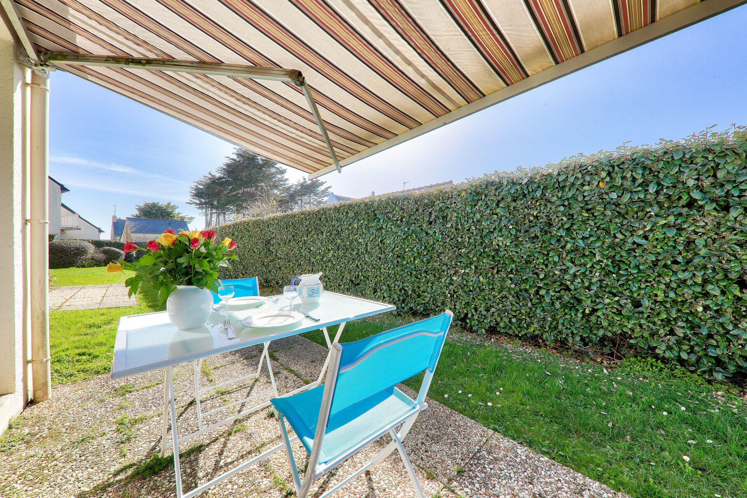 An outdoor patio with a table set for two, a chair, and a potted plant.