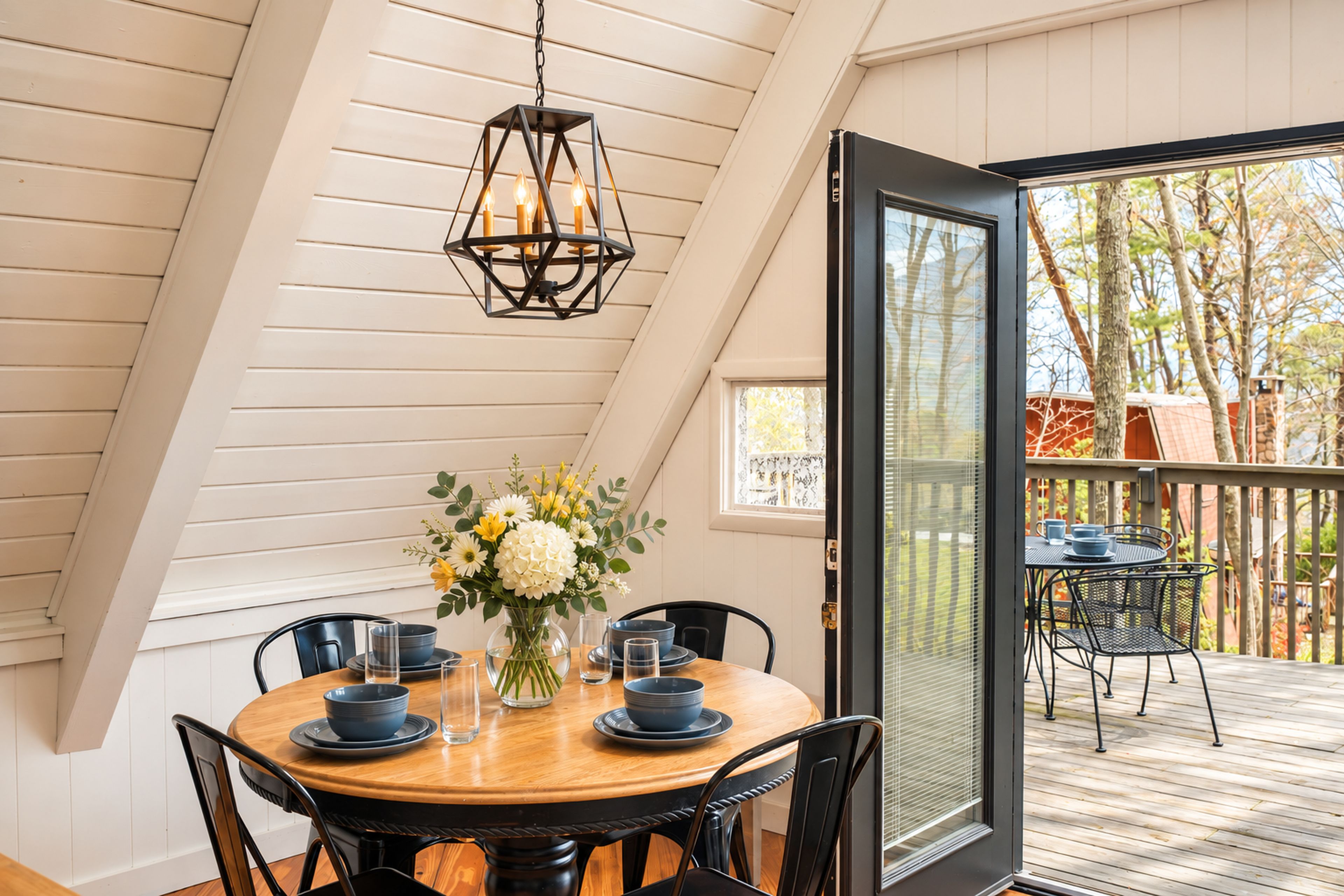 Un coin repas avec une table ronde, des chaises, un vase de fleurs et un luminaire suspendu.
