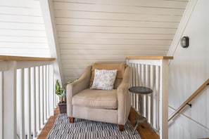 Une chaise avec un coussin, placée dans un couloir doté de rampes en bois et surmonté d’un tapis à motifs.