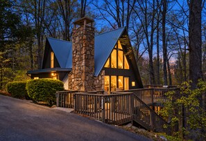 Une cabane moderne dotée d’une cheminée en pierre, de grandes fenêtres et d’une terrasse en bois.