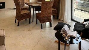 Een moderne woonkamer met een groot raam, rieten stoelen, een eettafel en hanglampen.