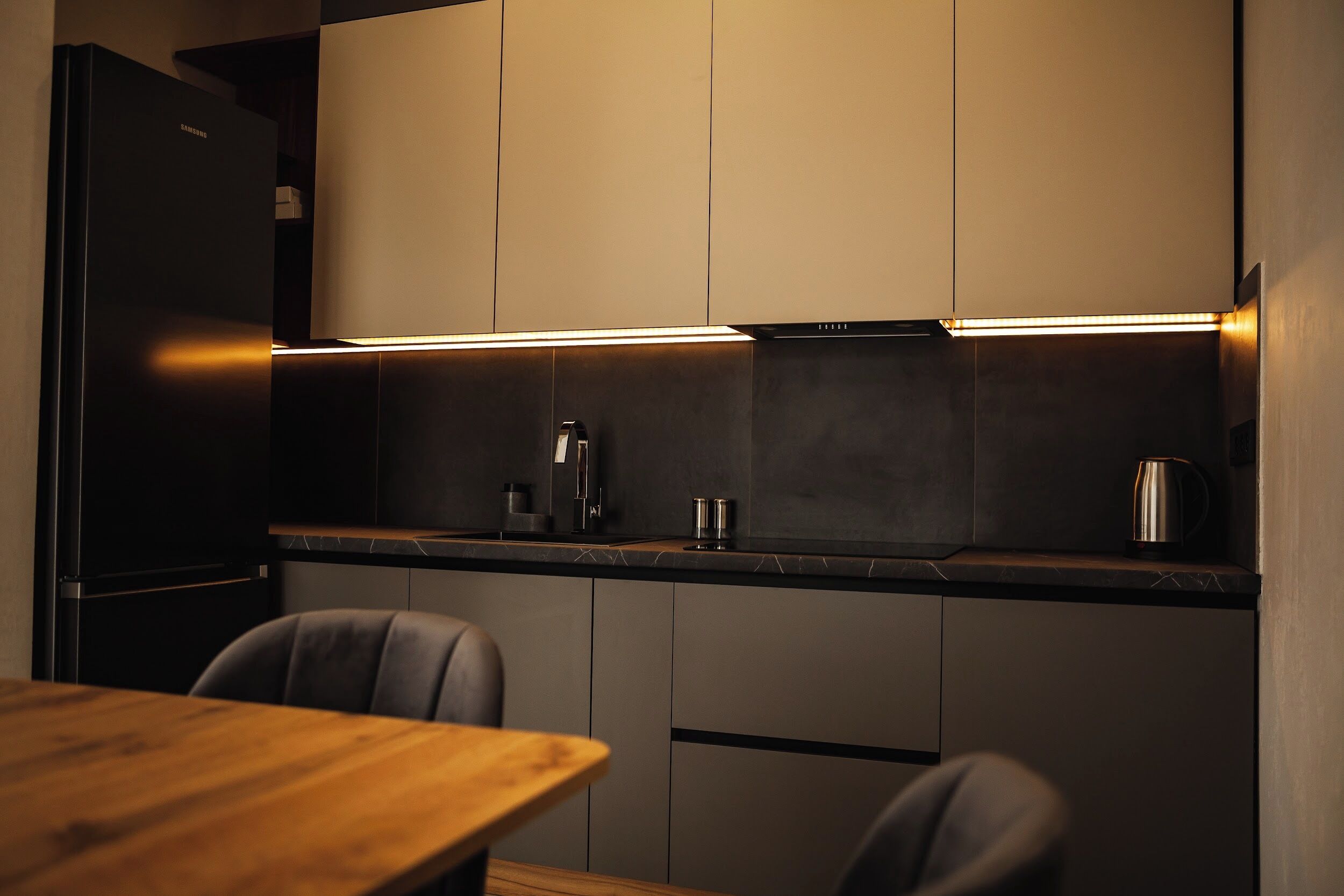 Una cocina moderna con armarios oscuros, una mesa de comedor de madera y un hervidor de acero inoxidable.