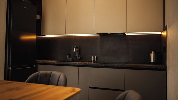 A modern kitchen with dark cabinetry, a wooden dining table, and a stainless steel kettle. - EcoBerghaus (Bukovel)