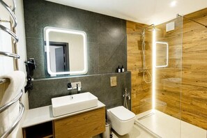 A modern bathroom with a large mirror, a white sink, a toilet, and a glass-enclosed shower area.