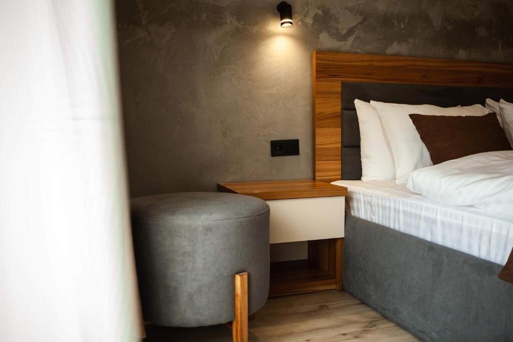 Una camera da letto moderna con una testiera in legno, una panca imbottita grigia e un comodino con una lampada.