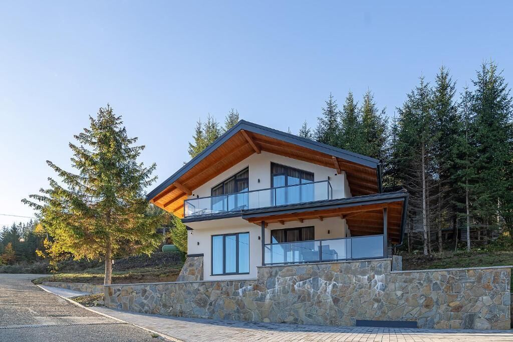 A modern two-story house with a stone facade, large windows, and a wooden roof.