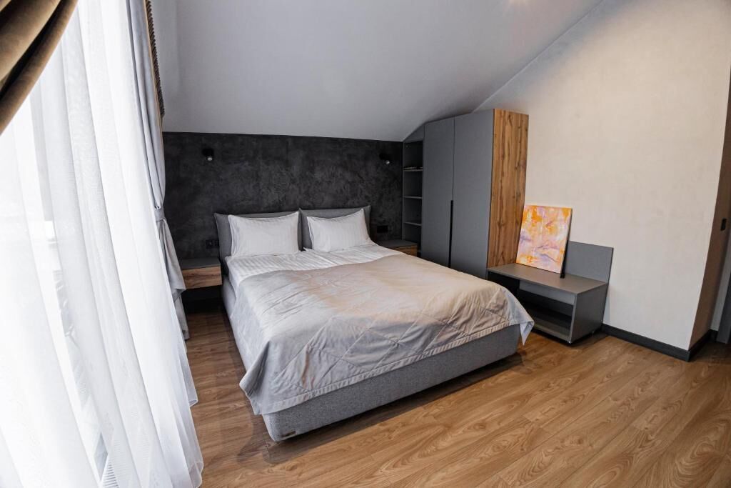 A modern bedroom with a large bed, a wooden floor, a dark headboard, and a grey wardrobe.