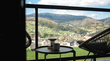 A view from a balcony with a table and chairs, overlooking a valley with houses and mountains.