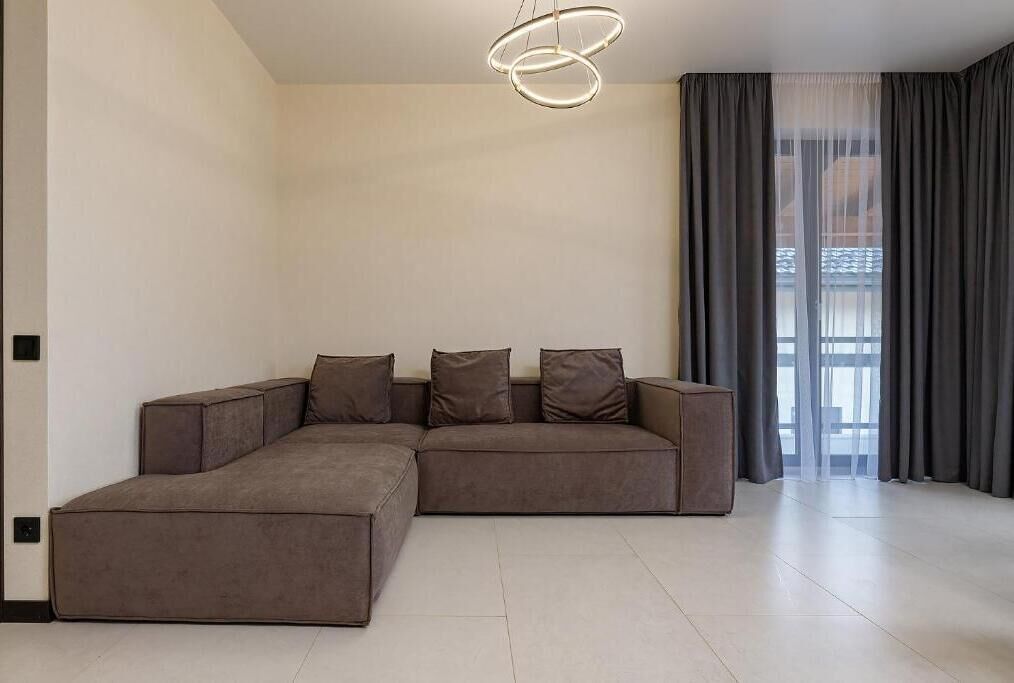 A modern living room with a sectional sofa, a pendant light, and a large window with curtains.
