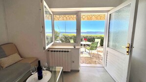 A compact living space with a glass table, a sofa, and a view of the outdoors through a large window. - Apartman Kate 1 (Dramalj)