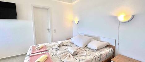 Una cama bien hecha con toallas, una mesita de noche con lámpara y un televisor en la pared.
