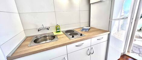 Una cocina moderna con armarios blancos, un lavamanos de acero inoxidable, una estufa a gas y un refrigerador.