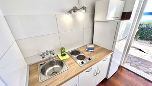 A compact kitchen with white tiles, a stainless steel sink, a wooden countertop, and a small stove. - Apartman Kate 1 (Dramalj)