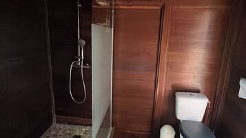 Une salle de bain en bois équipée d’une douche, de toilettes et d’une petite poubelle.
