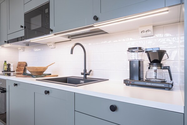 Una cocina moderna con microondas integrado, cafetera y lavamanos.