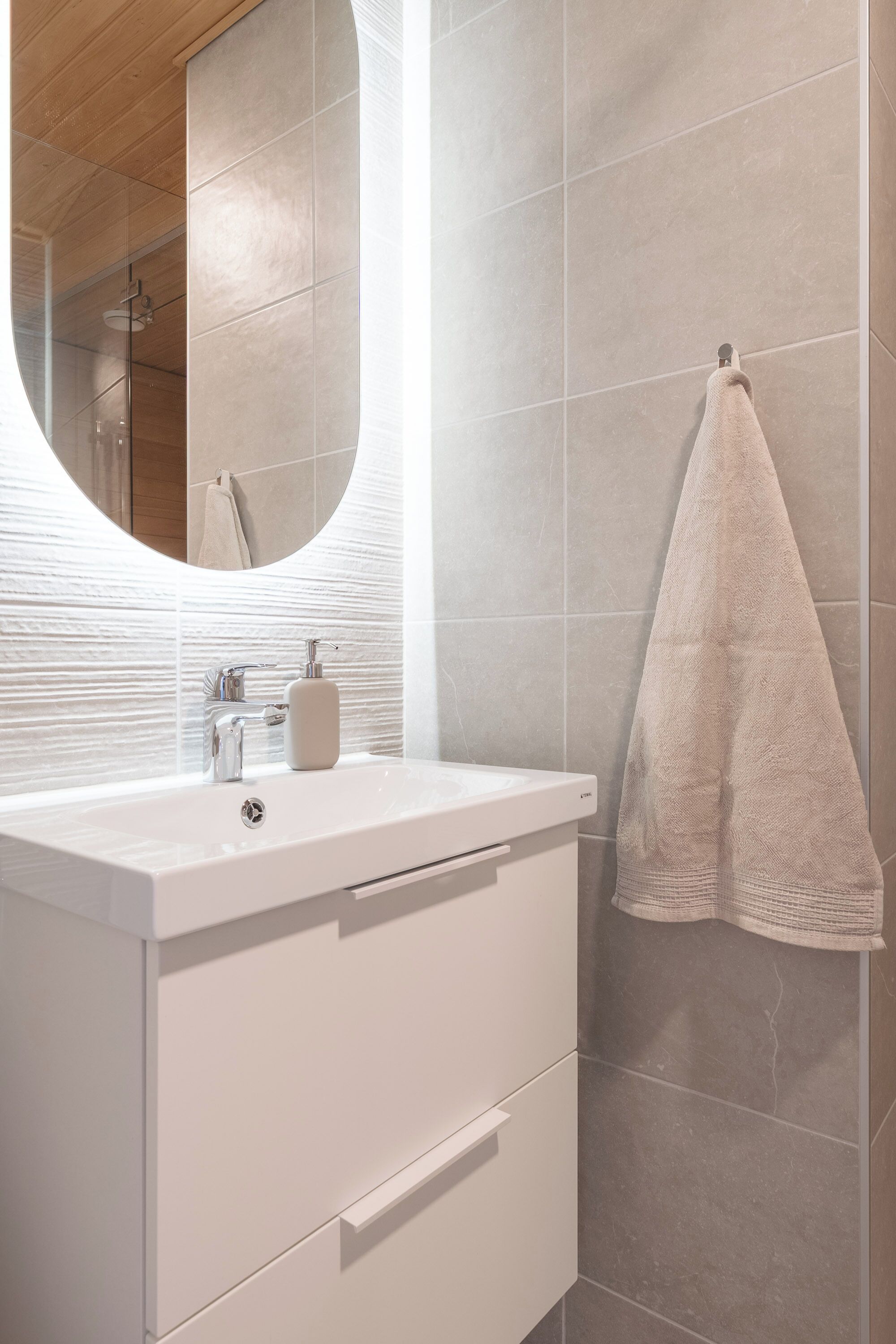 A modern bathroom with a white vanity, a round mirror, and a towel hanging on the wall.
