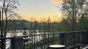 Un espace extérieur aménagé avec une table et des bancs, offrant une vue sur une étendue d’eau et sur le paysage urbain en arrière-plan.