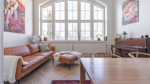 Un salon chaleureux avec une grande fenêtre en arc de cercle, un canapé en cuir, une table à manger en bois et un piano.