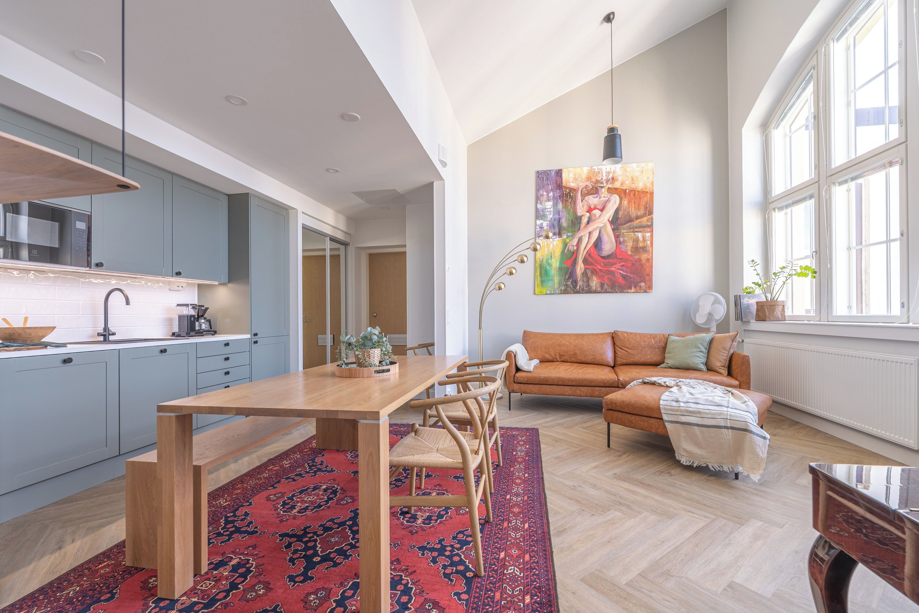 A spacious living area with a wooden dining table, a sofa, and a large window providing natural light.