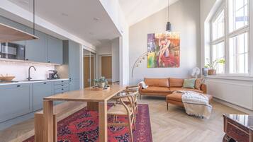 A spacious living area with a wooden dining table, a sofa, and a large window providing natural light.