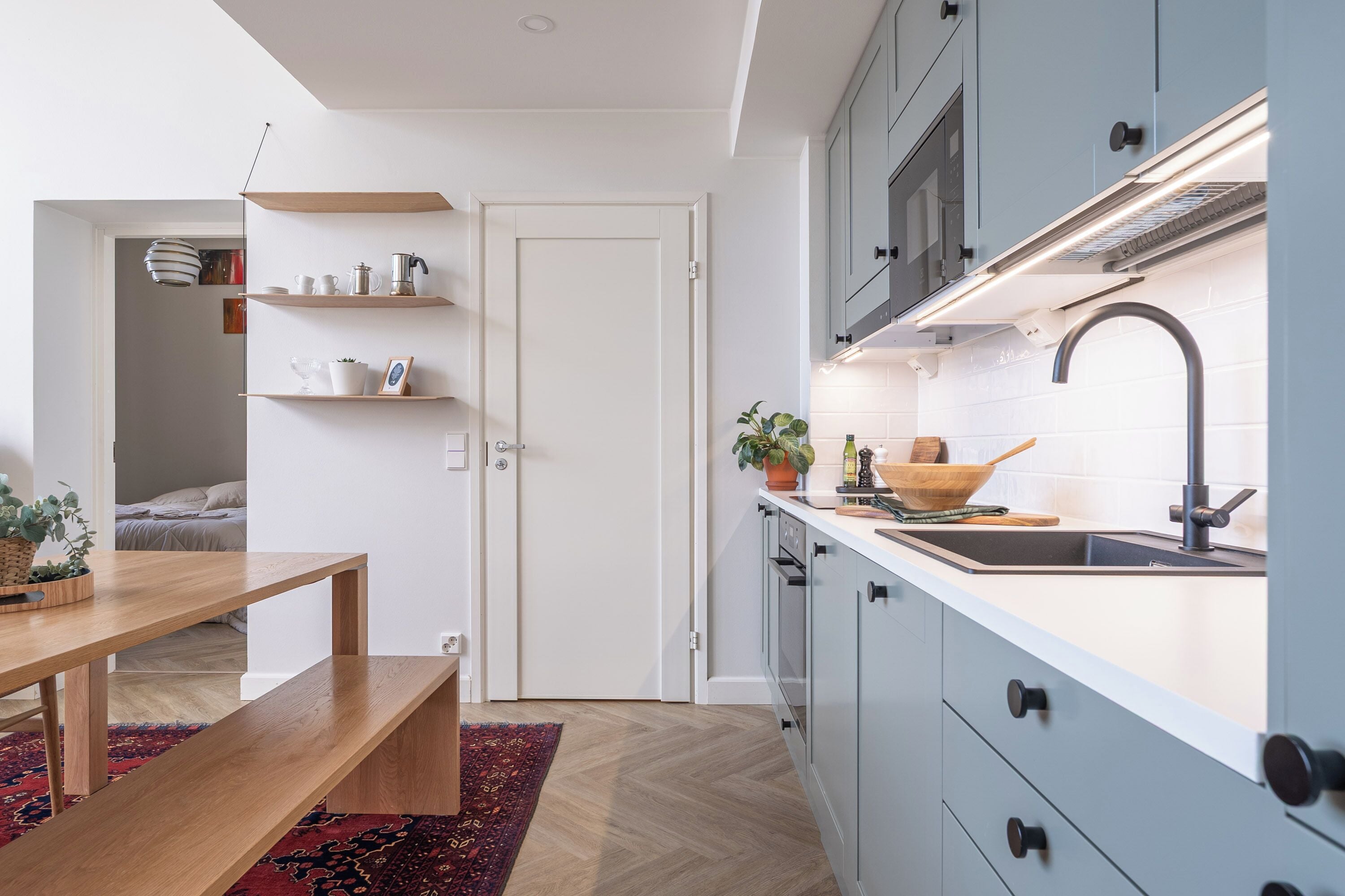 Eine moderne Küche mit weißen Schränken, einem Holztisch und einem roten Teppich mit Muster.
