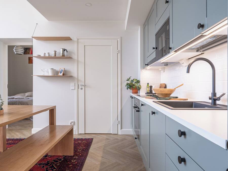 Eine moderne Küche mit weißen Schränken, einem Holztisch und einem roten Teppich mit Muster.