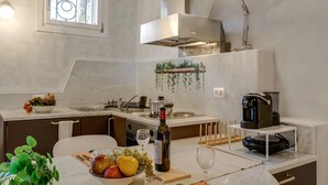 A modern kitchen with a dining area, featuring a built-in stove, a coffee machine, and a wine bottle on the counter. - Lory-cosy Gardone Old Town&vittoriale (Gardone Riviera)