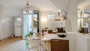 A modern kitchen with white cabinetry, a dining area with a white table and chairs, and a view of the outdoors through a glass door. - Lory-cosy Gardone Old Town&vittoriale (Gardone Riviera)
