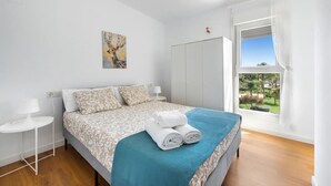 Un dormitorio con una cama, una ventana con vistas, un cuadro en la pared y una mesita de noche con una lámpara.