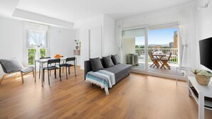 Amplia sala de estar con un sofá gris, una mesa de comedor con sillas y un balcón con vistas a la ciudad.