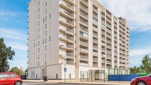 Un edificio residencial de varios pisos con balcones, un área de estacionamiento y cielo despejado.